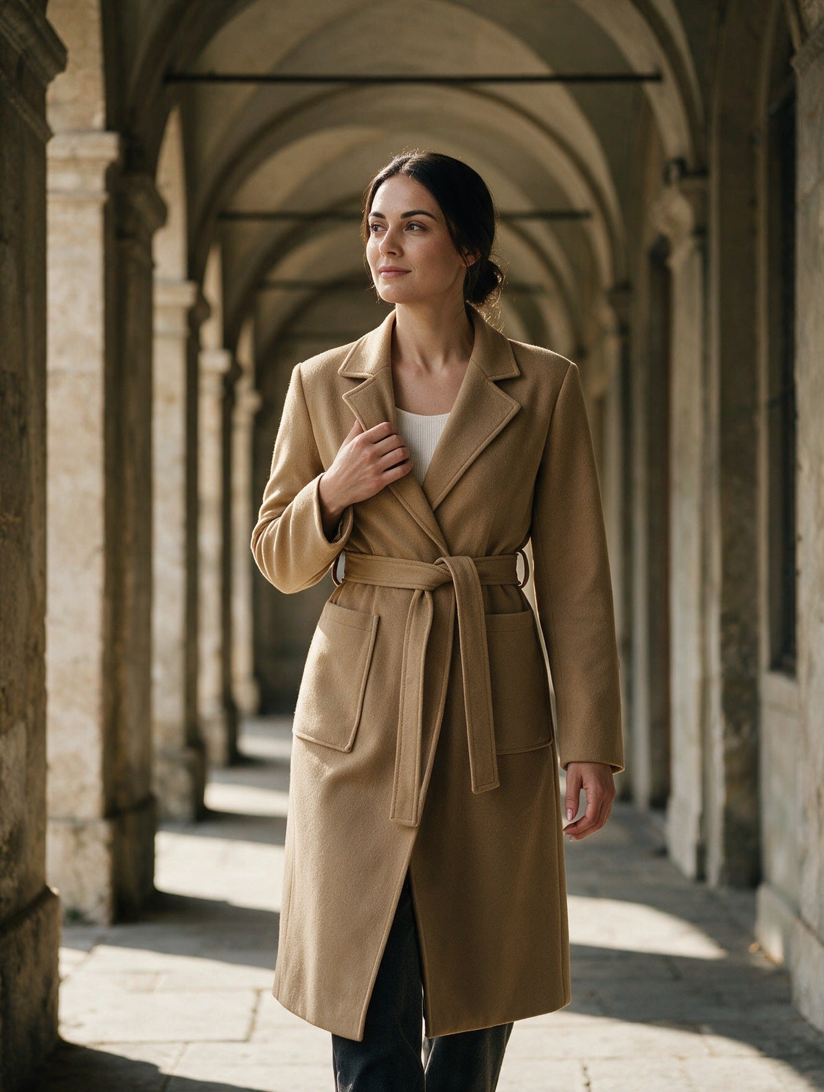 Sofia wears a camel-coloured coat beneath a stone portico.